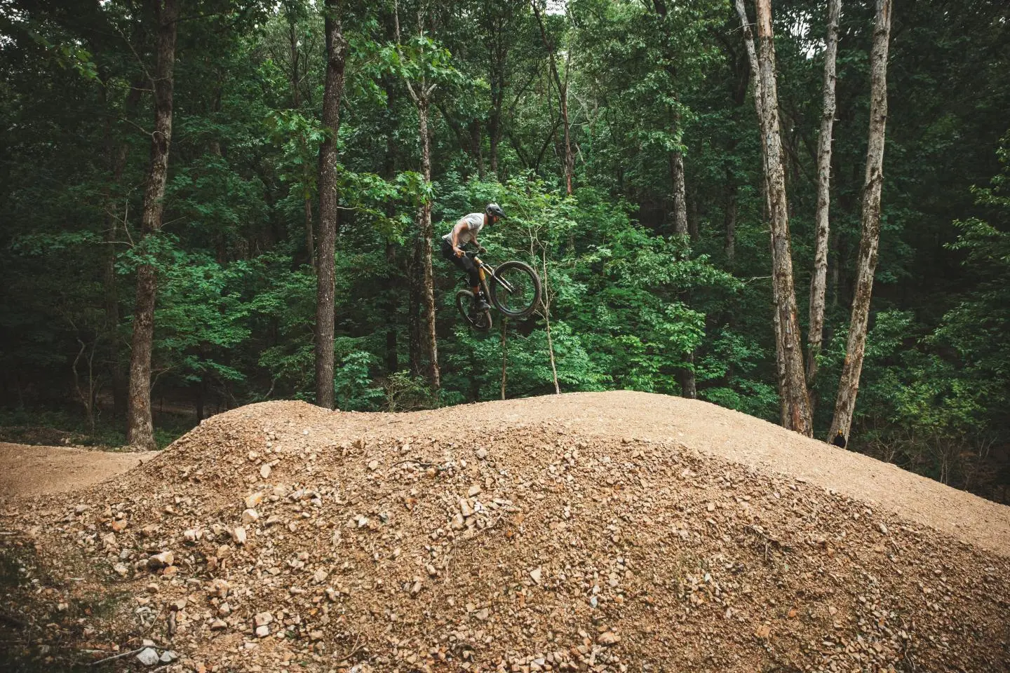 A mountain biker clearing a dirt jump in the hardwood forest at OZ Trails Bike Park